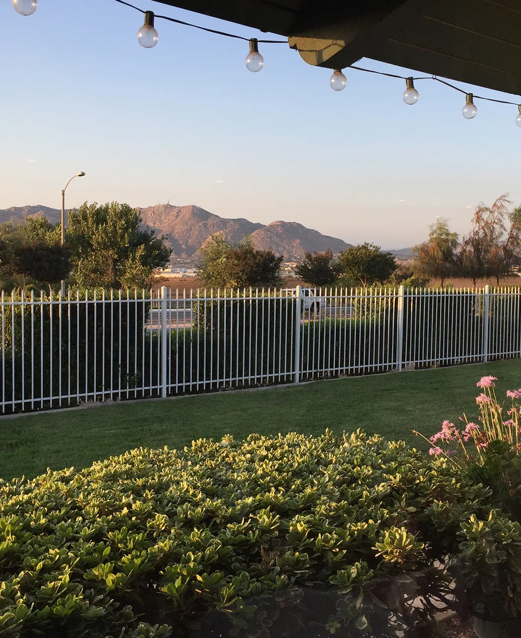 Scenic outdoor patio view with string lights, garden landscaping, and mountain backdrop at Orangecrest Club venue